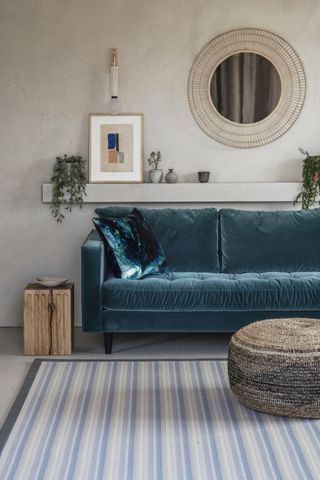 A living room with a blue velvet sofa and a patterned wool rug