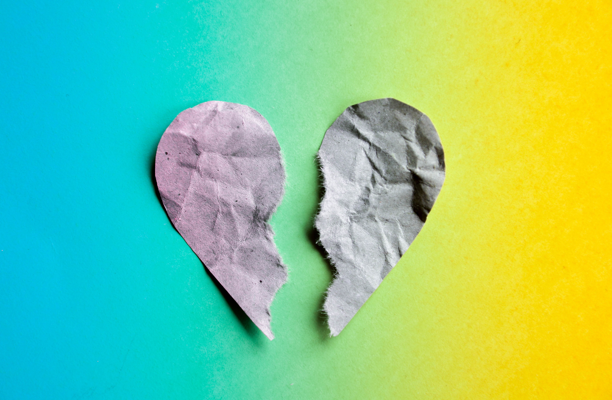 Broken paper heart on a fading color background, mental wellbeing