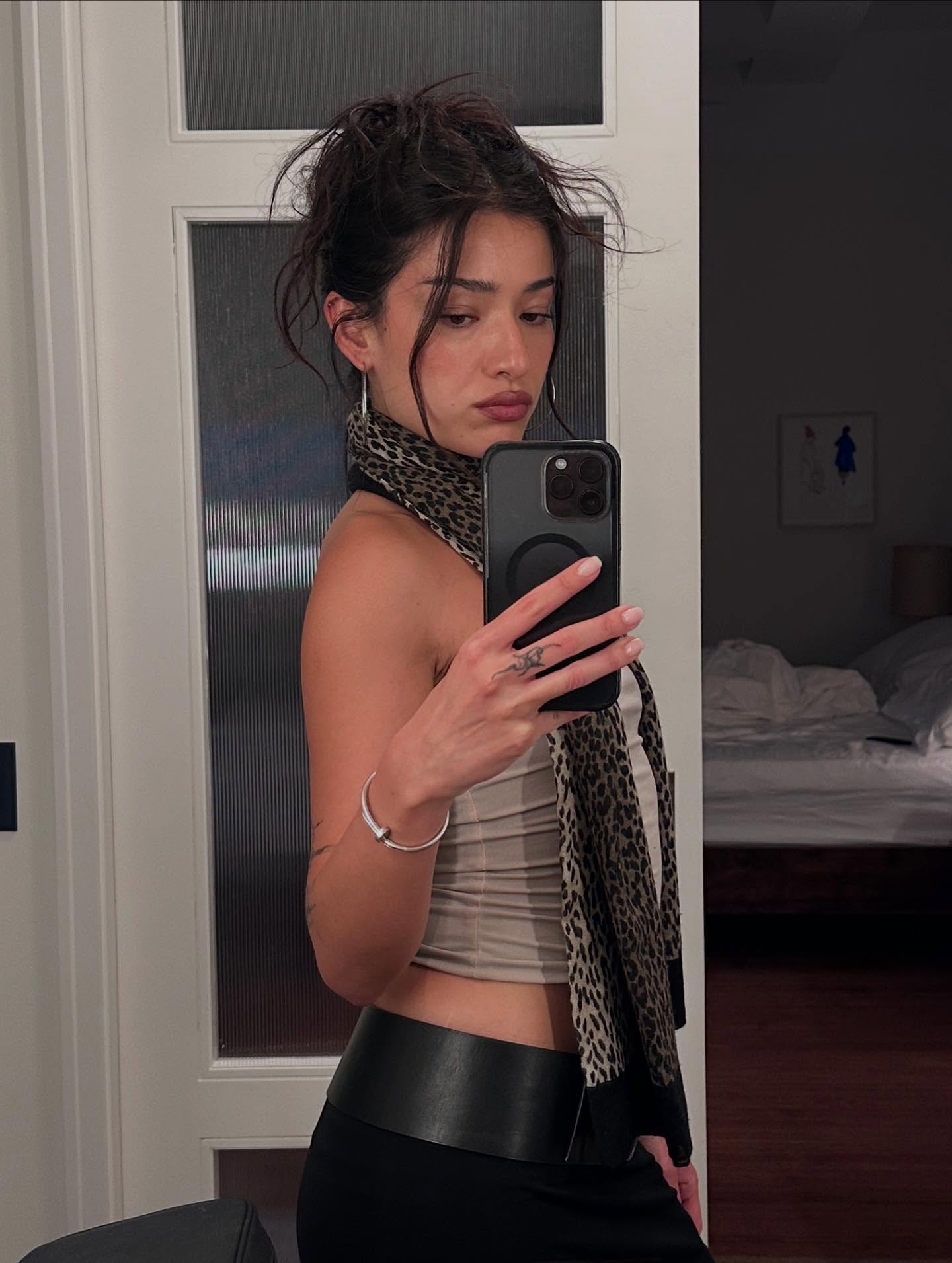 A mirror selfie of Yasmin Istanbouli wearing a tank top, cheetah scarf, wide leather belt, and messy bun.