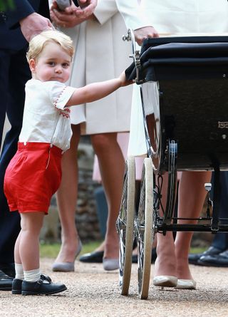 Prince George holding pram with Princess Charlotte