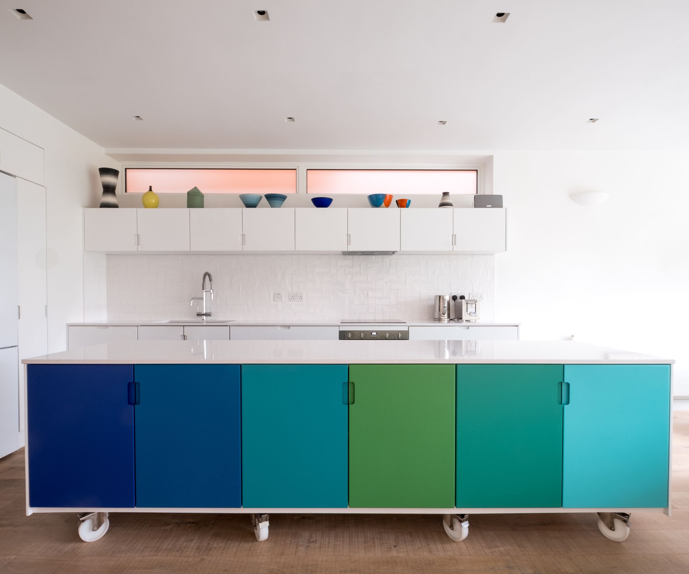 Custom designed kitchen island on industrial castor wheels in open plan living space. Island is made from MDF and is painted in blue and green ombre colours.