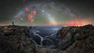 Person stands on rocky cliffs overlooking a calm sea under a vibrant, star-filled night sky with colorful nebulae and galaxy arches