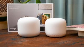 Two white Google Nest Wifi devices on a table in front of their retail packaging