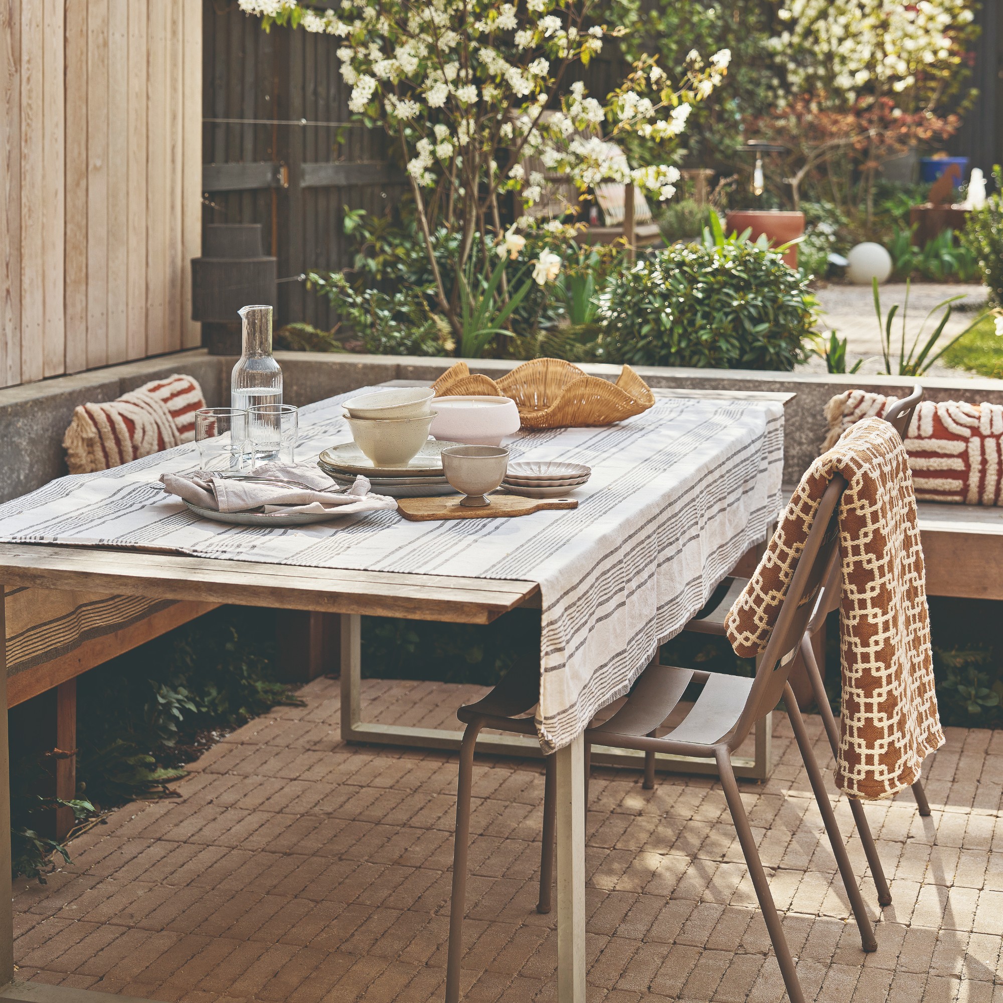 A garden with an outdoor dining area with a set dining table, a chair and a built-in bench