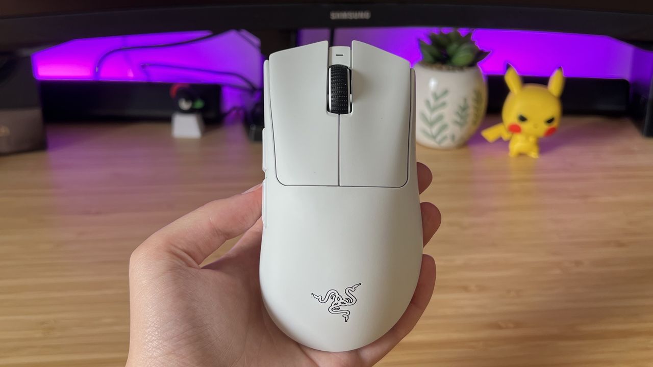 Hand holding Razer DeathAdder V4 Pro gaming mouse above a wooden desk with purple backlighting
