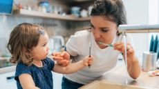 Mother and daughter baby girl brushing their teeth together at their kitchen sink