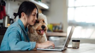 A woman and a dog browse the internet on a laptop at the table