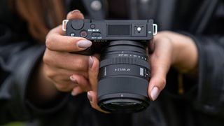 Viltrox AF 90mm F2.2 EVO lens attached to a Sony camera, held downwards by a photographer