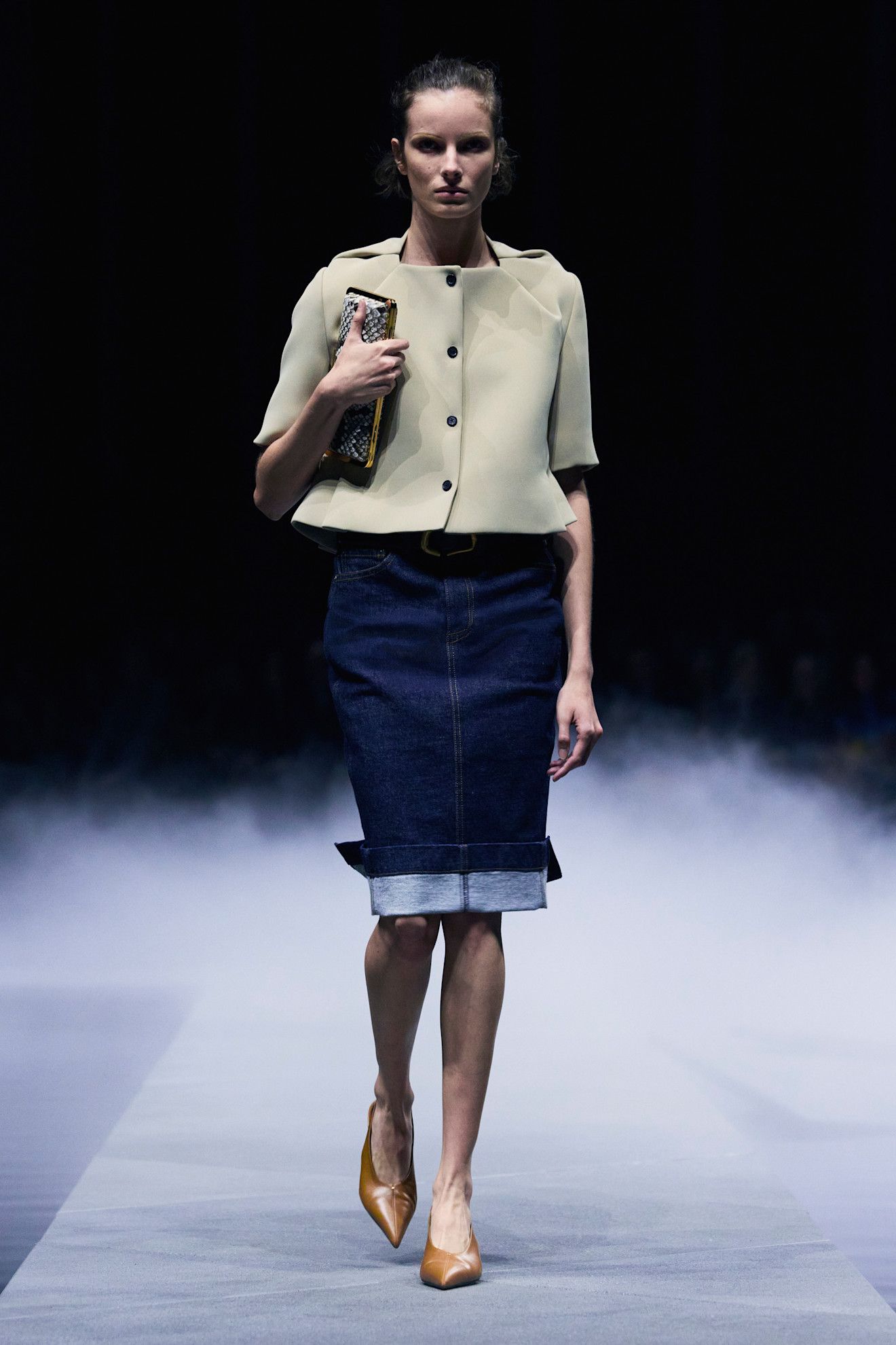 A model at the spring/summer 2026 show for Khaite wearing a cropped khaki jacket and knee-length denim pencil skirt.
