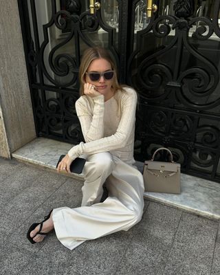 Influencer styles cream trousers with a cream blouse and a burgundy bag.