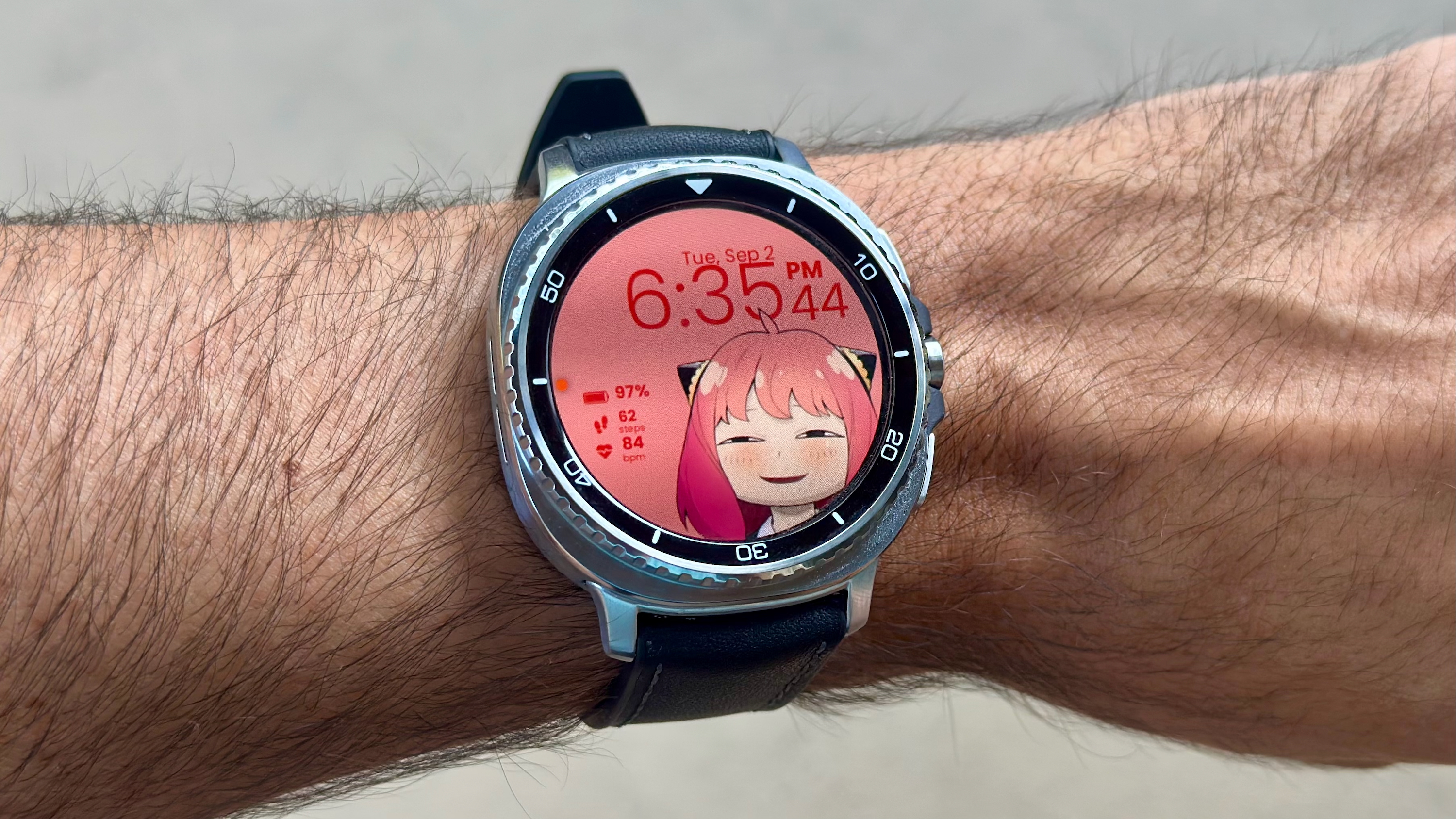 The Samsung Galaxy Watch 8 Classic on a person's wrist, showing a custom watch face with Anya from the anime Spy x Family smiling below the time.