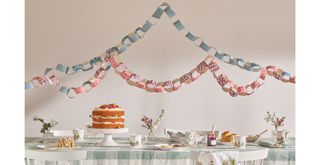 party table with gingham tablecloth and cakes on cakestands with paper chains hanging above