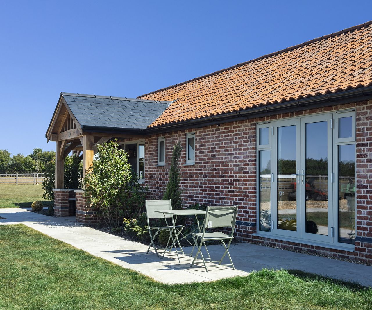 A small patio with bistro table in front of a pitched roof oak frame home clad in red brick