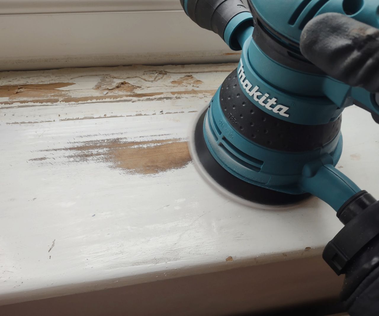 An orbital sander removing paint from a windowsill