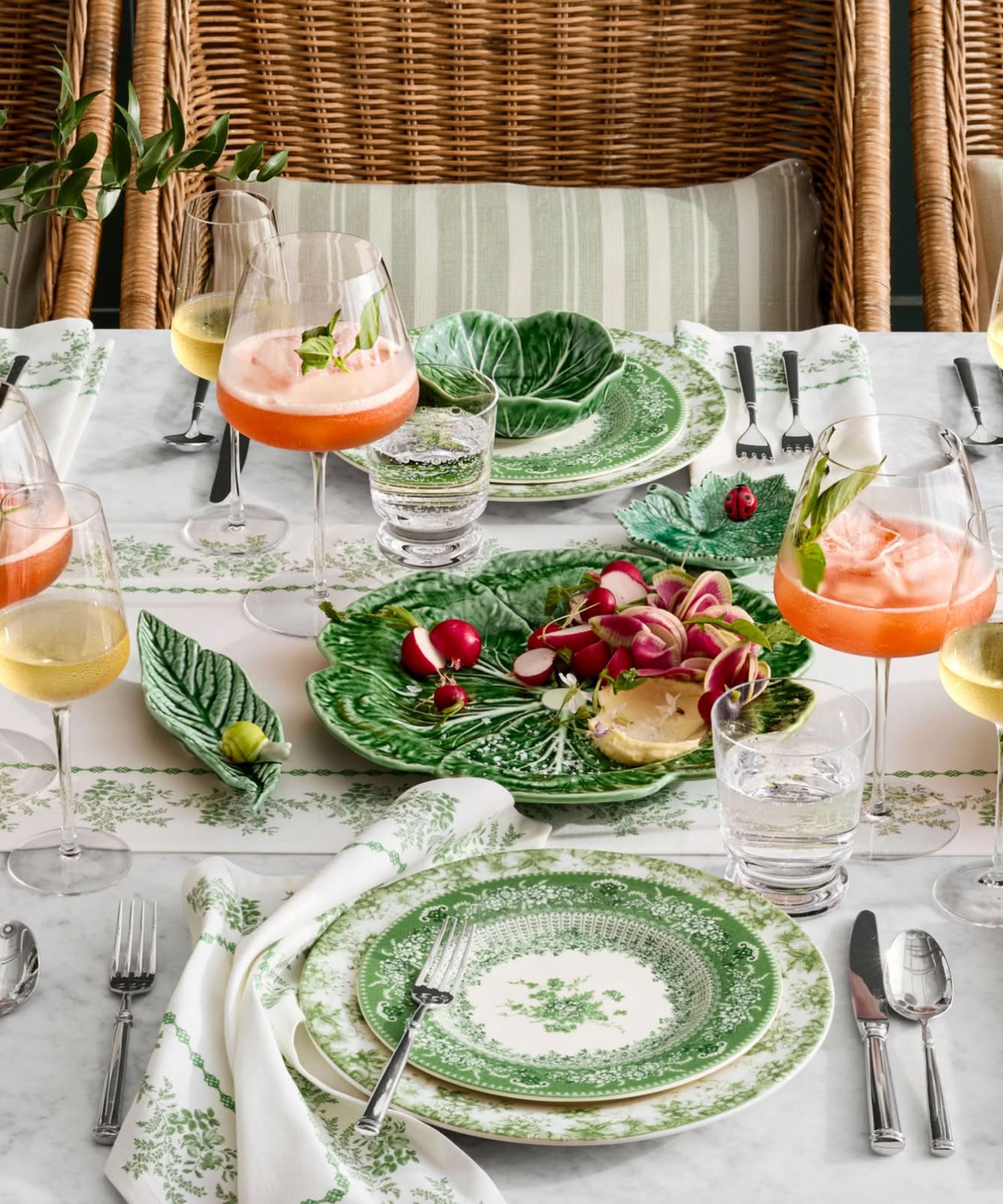Green themed tablescape with leaf shaped dishes, vintage style plates, rattan chairs and pink cocktails