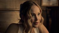 Jennifer Lawrence, wearing a white tank top and hair pulled back, sitting at dinner in 2023's comedy No Hard Feelings.