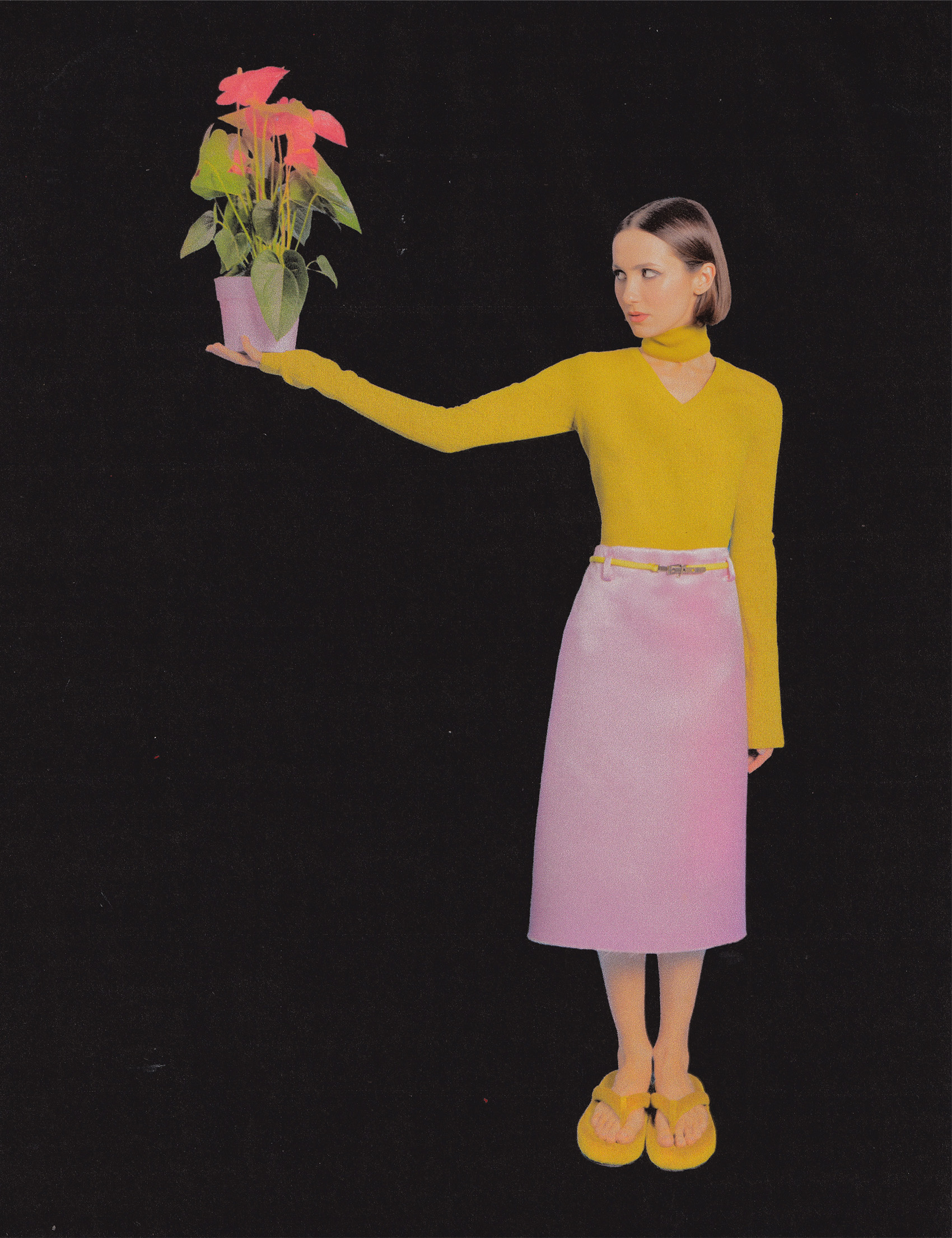 Maude Apatow photographed by Dana Trippe for Who What Wear. She is standing against a black backdrop holding a plant in her right hand. She is wearing a yellow long sleeve top and pink midi skirt.