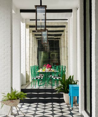 Rectangular clear patio light within black metal edged lantern suspended from ceiling, black and white tiles, green table set, mirror reflecting