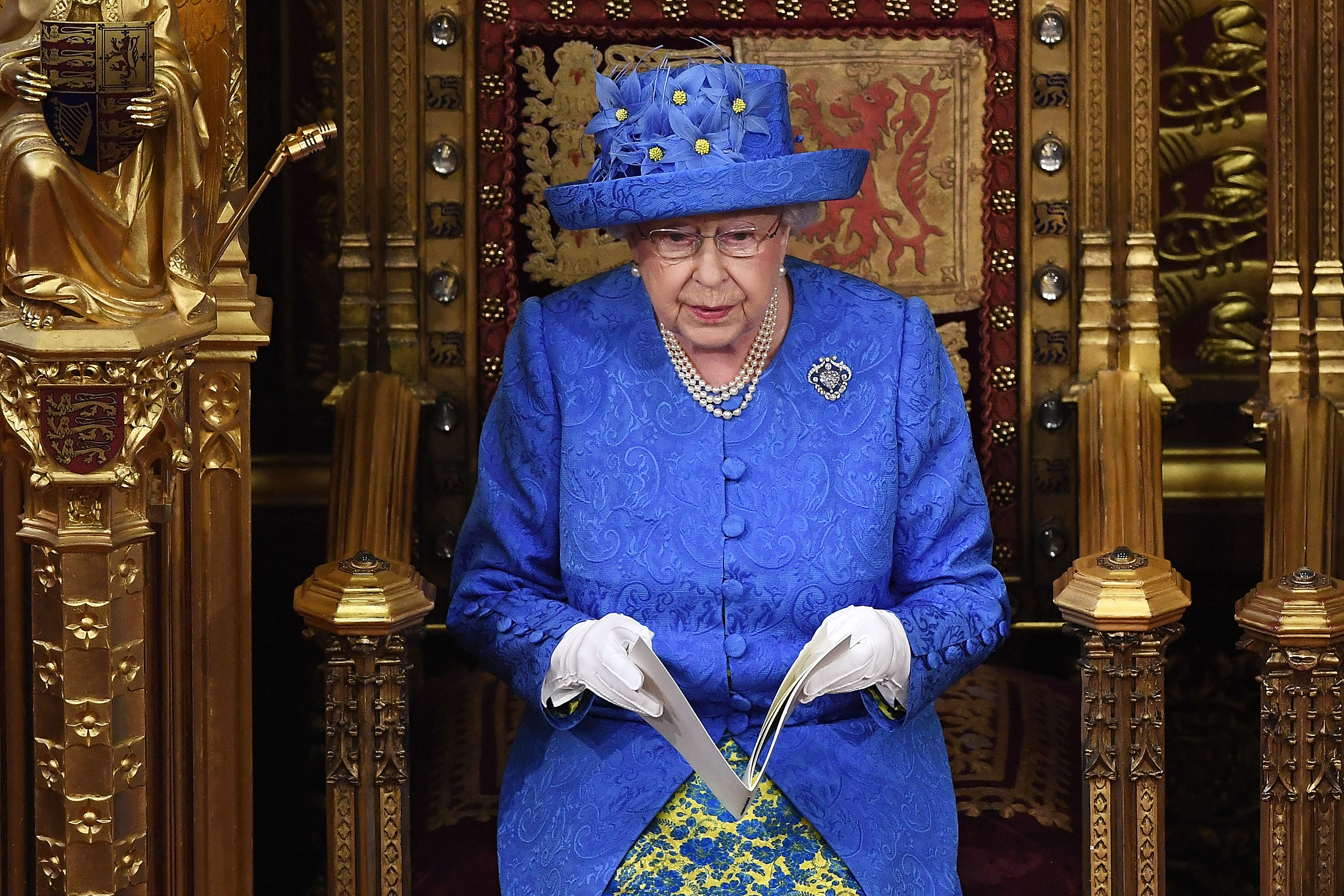 Queen Elizabeth sitting in a gold chair wearing a blue coat and hat