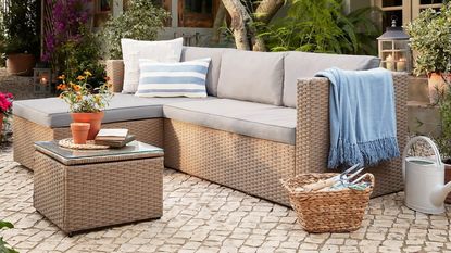 A rattan-effect garden sofa with light grey cushions on a contemporary patio