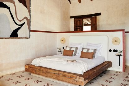 A rustic bedroom with geometric tiles, a low wooden bed and lime-wash effect walls
