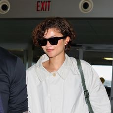 Zendaya heads to the airport in a white The Row trench coat, a white skirt, and black loafers, tapping into two Spring 2026 It-Girl trends