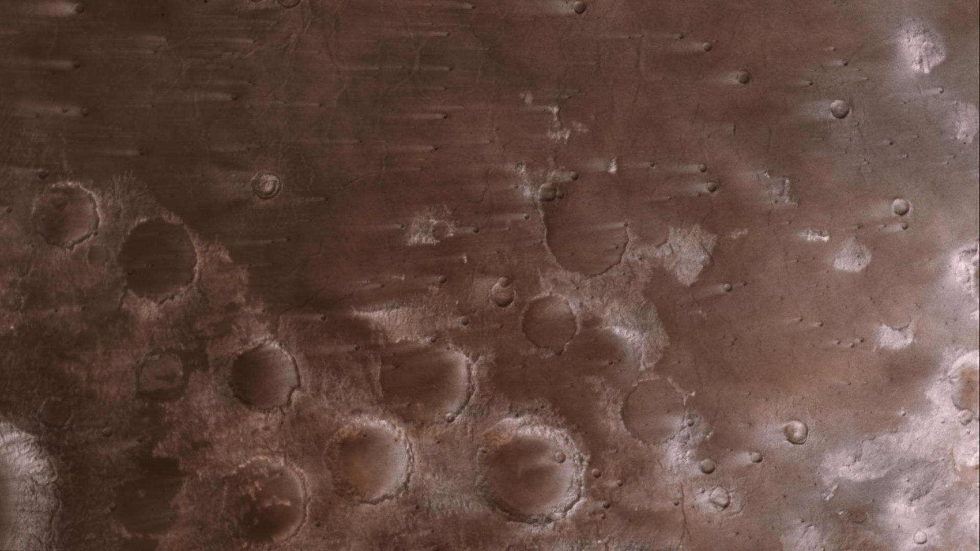 A reddish planet's surface with craters and streaks that make it almost look blurry.