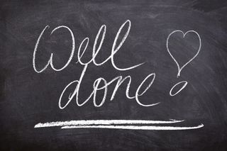 The words "Well Done" are handwritten in chalk on a blackboard. There is a heart next to them, also written in chalk.