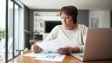 An older woman works on financial paperwork at her dining room table.