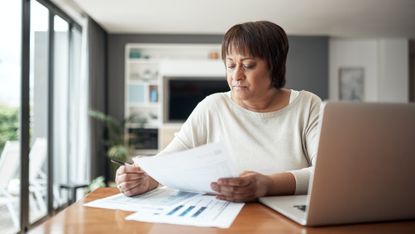 An older woman works on financial paperwork at her dining room table.