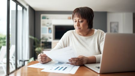An older woman works on financial paperwork at her dining room table.