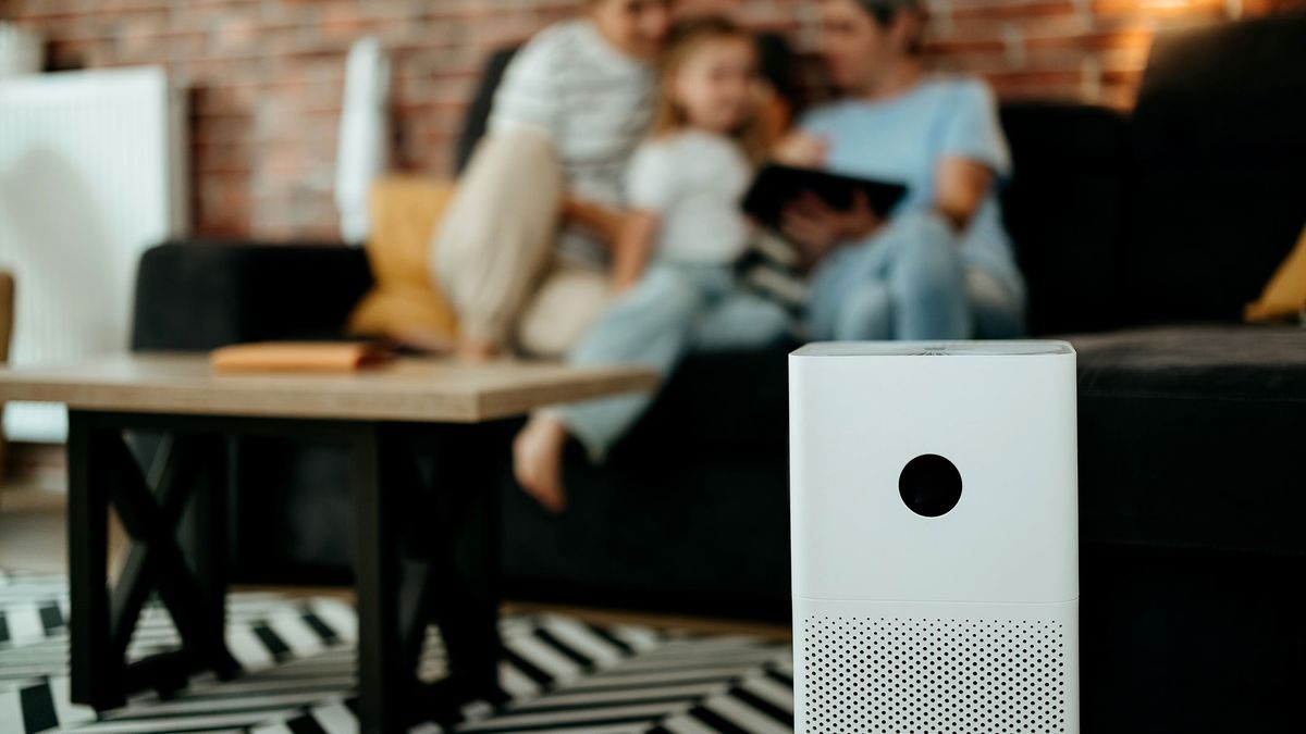 An air purifier standing in the middle of a living room, with a family sitting on a sofa behind it