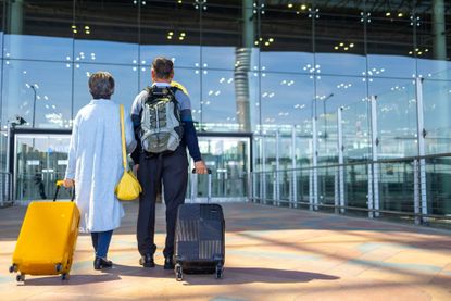 Asian senior couple wheeling luggage while walking into an airport terminal.