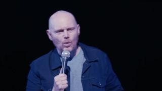 Bill Burr in a blue shirt, holding a microphone