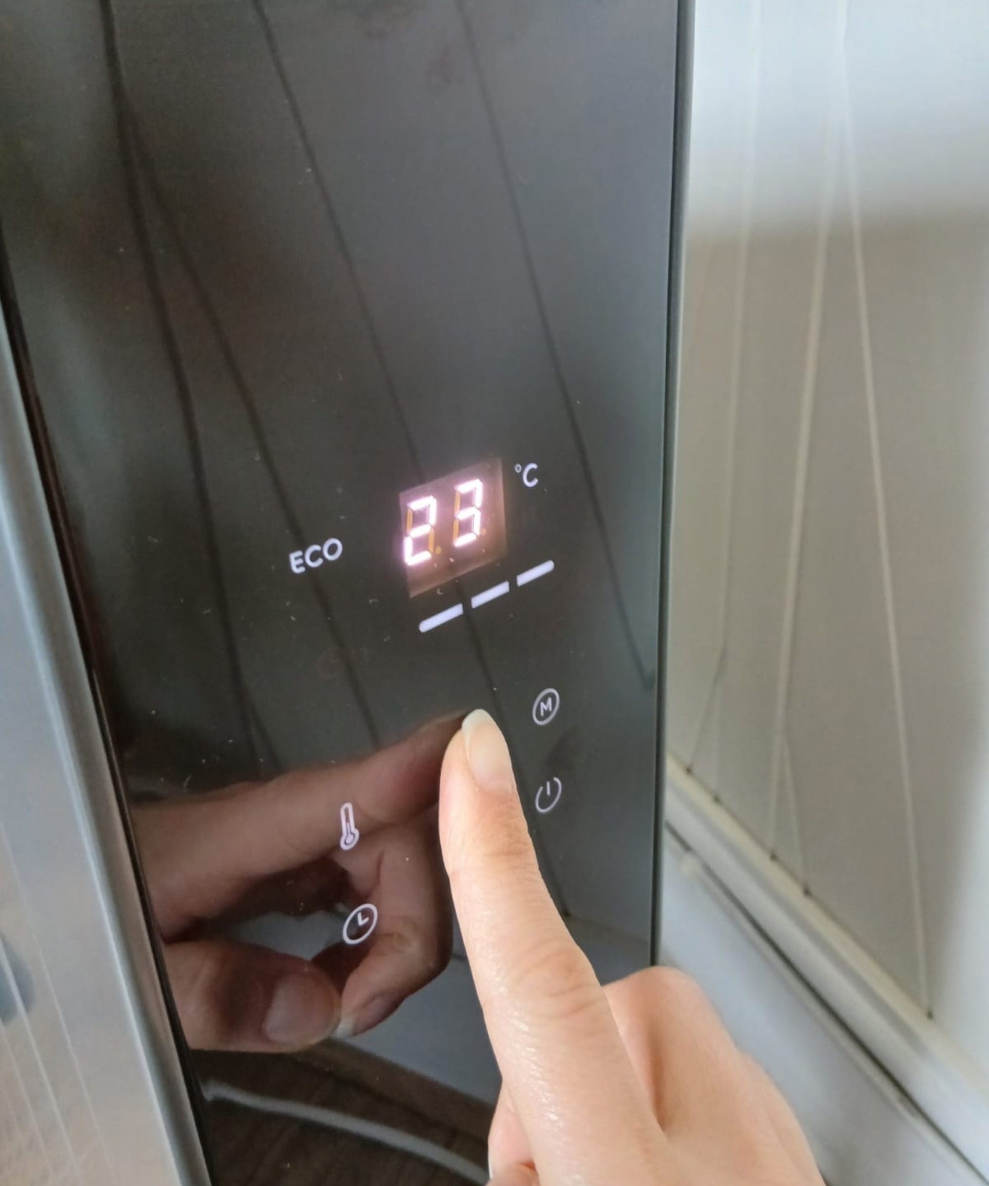 A woman's hand adjusting an LED screen on a digital portable heater
