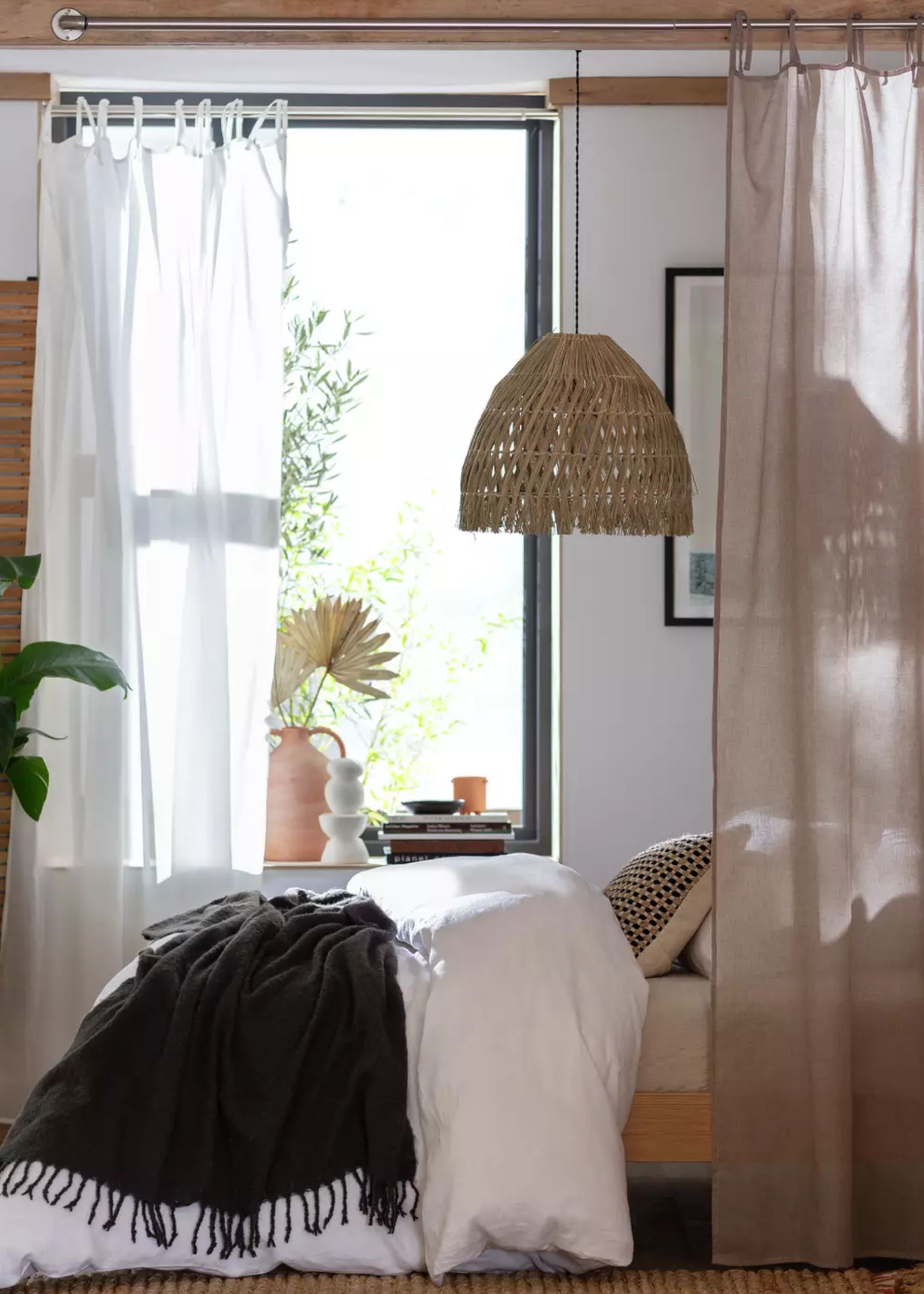 A bedroom with a bed and curtains next to the bed as well as beside the window. There is a pendant light hanging above the bed and on the bed are pillows as well as a throw.