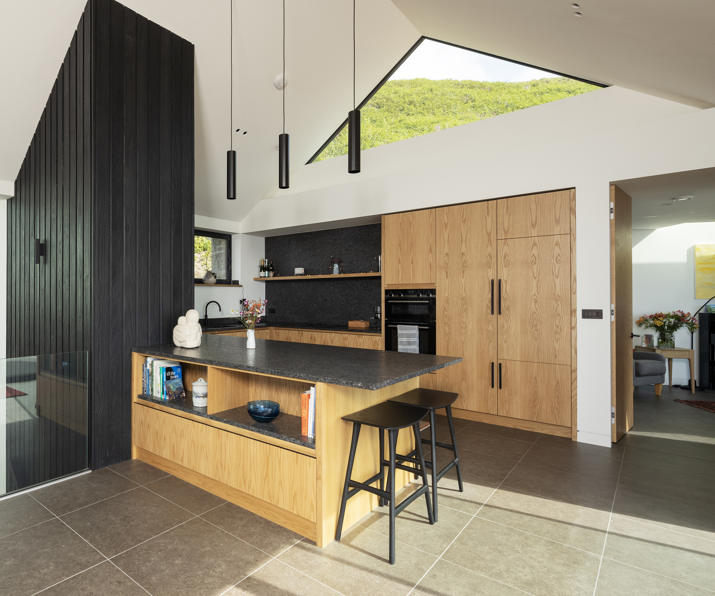 A wooden kitchen with black surfaces and pendant lights. With built-in appliances
