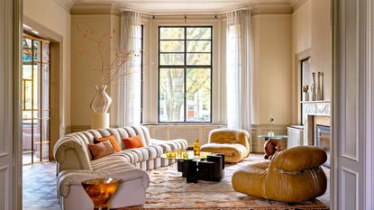 Butter yellow living room with curved sofa, tan leather accent chairs, dark wood and glass coffee table and patterned peach rug
