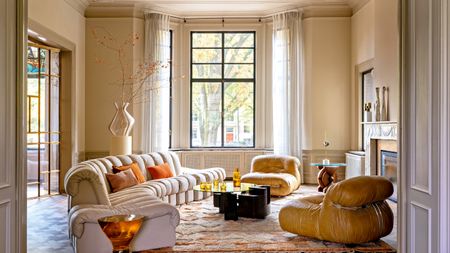 Butter yellow living room with curved sofa, tan leather accent chairs, dark wood and glass coffee table and patterned peach rug
