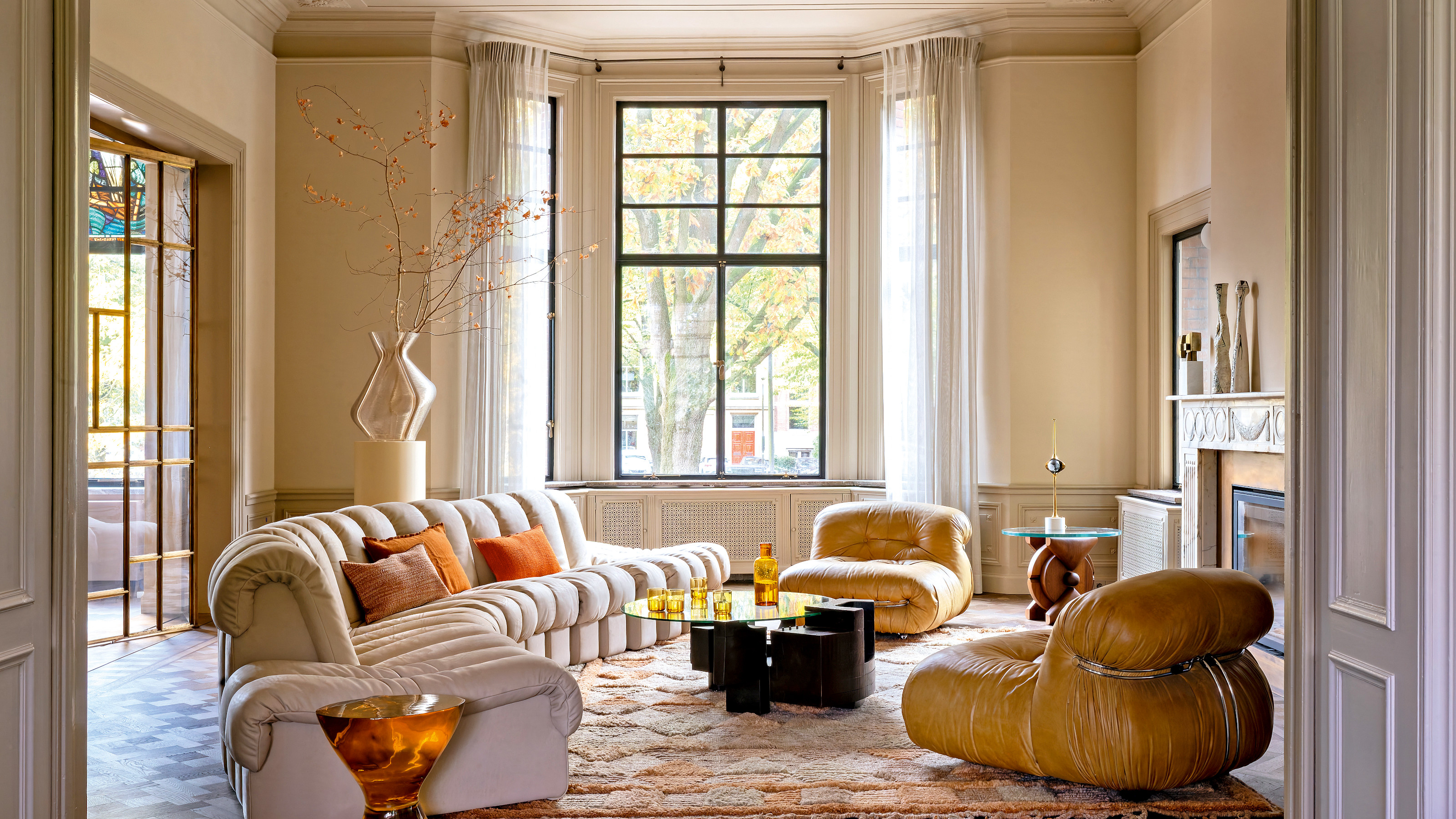Butter yellow living room with curved sofa, tan leather accent chairs, dark wood and glass coffee table and patterned peach rug