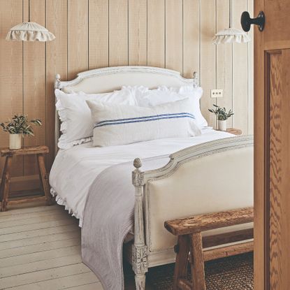 A wood-panelled bedroom with pendant ruffled lights on either side of the bed with rustic bedside tables and a bench at the foot of the bed