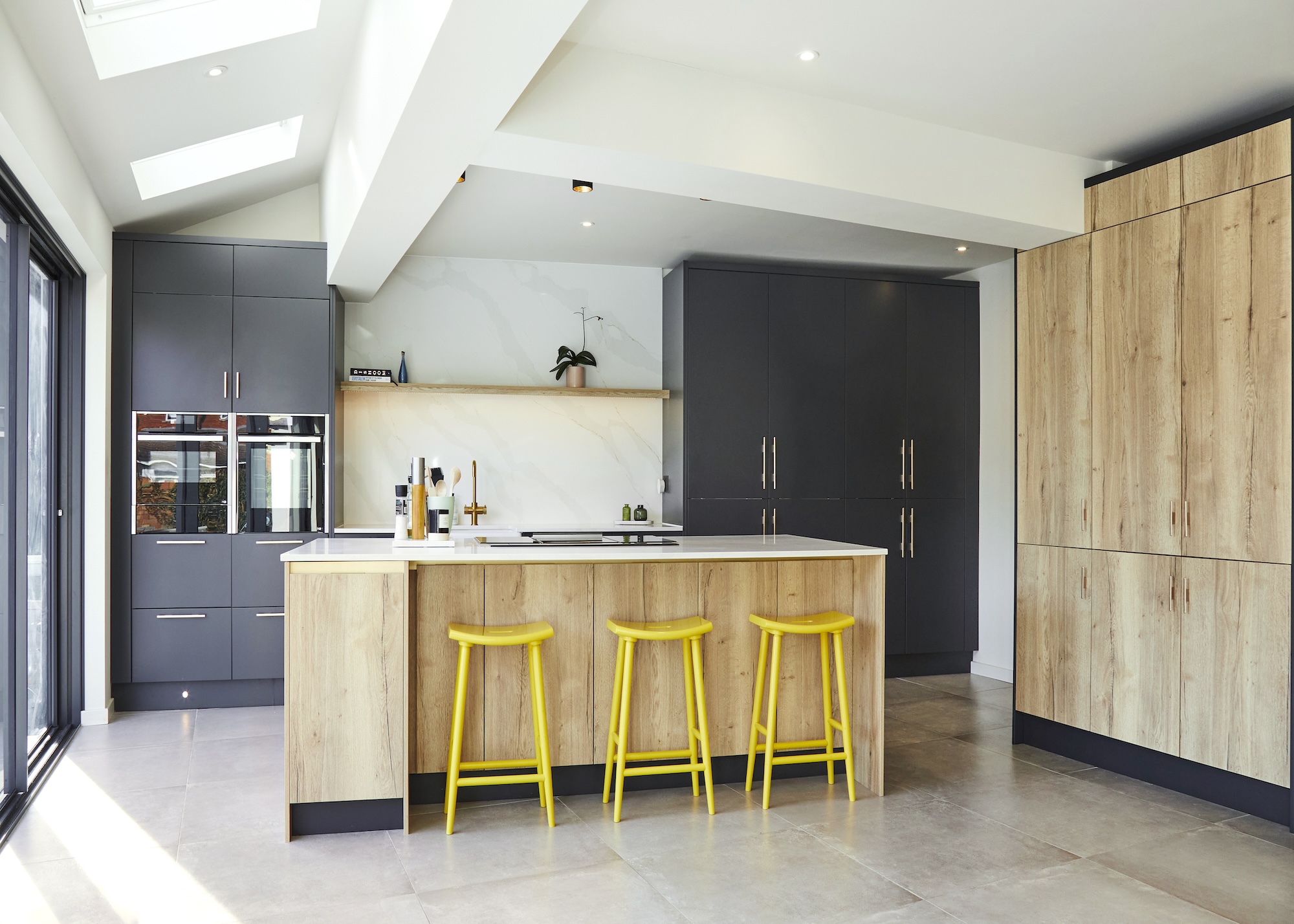 a modern kitchen with charcoal coloured cabinets mixed with pale wood units and an island with yellow bar stools