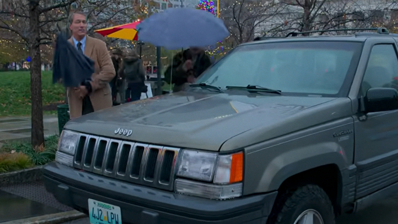 John Corbett holding an umbrella standing by a Jeep Cherokee with Missouri plates
