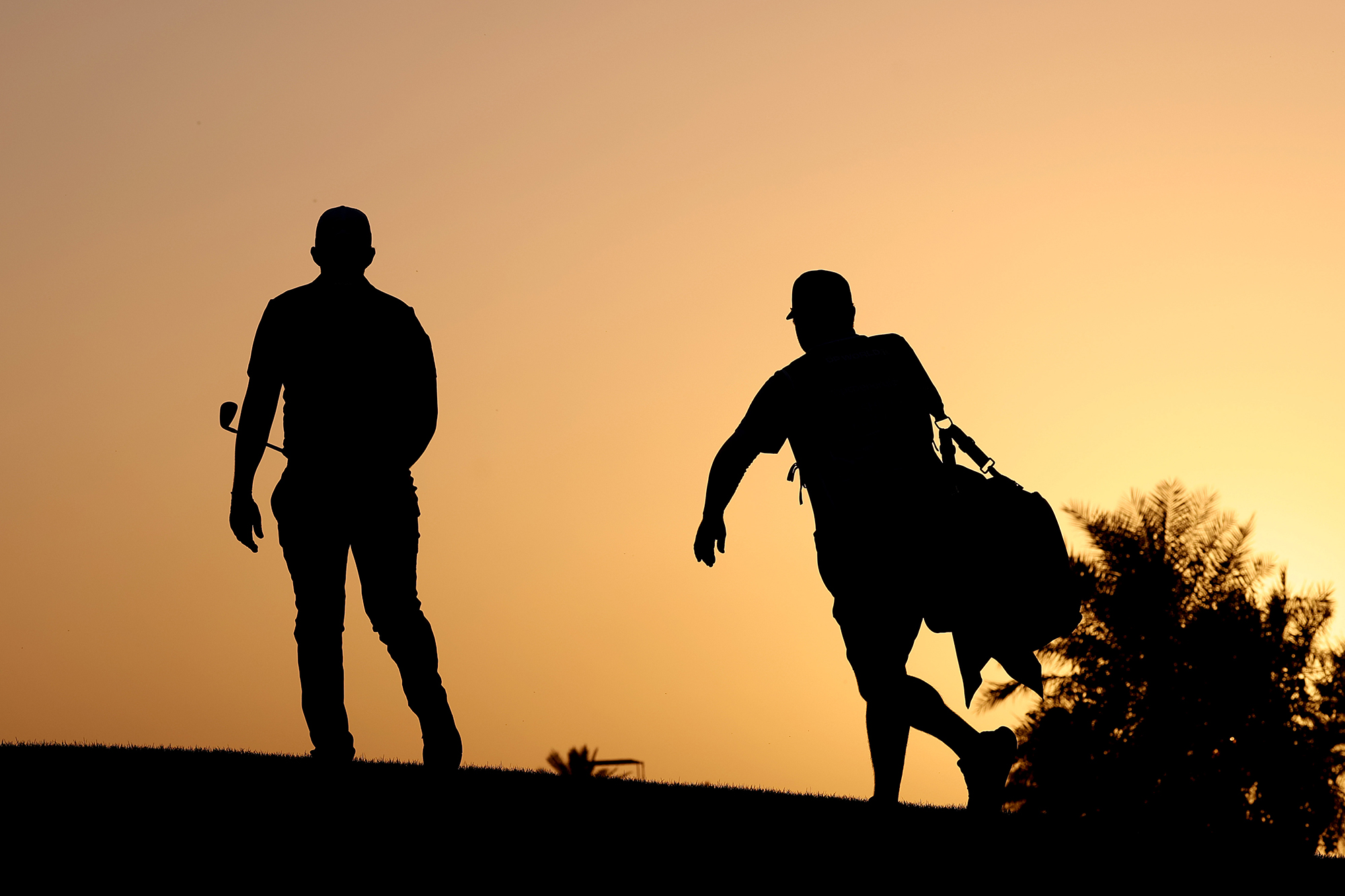 A player with his caddie, who is carrying the bag, silhouetted against the evening sun