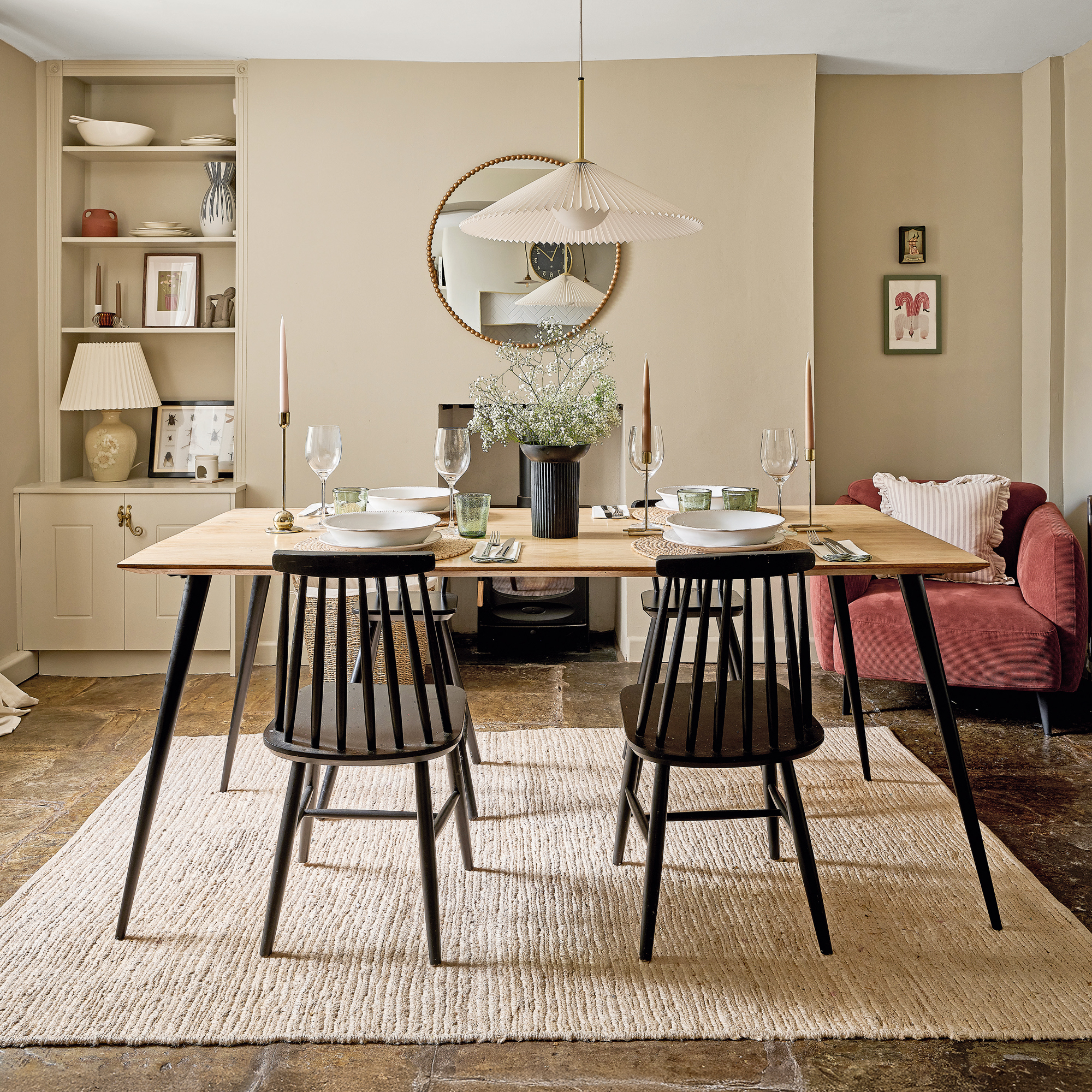 a neutral dining room with a painted black wooden table and chairs, slate flooring and a terracotta velvet upholstered armchair