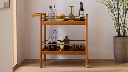On of the best bar carts, a West Elm mid-century bar cart in a home, stocked with gin, wine, and cocktail equipment