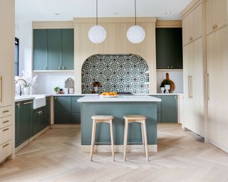 Modern kitchen with large green painted wooden island, two stools and tile stove backsplash