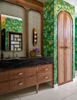 bathroom with cabinets and built in cabinet, green fern wallpaper, stone floor, mirror, black countertop