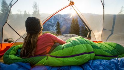 Woman in a sleeping bag looking at the view out the tent