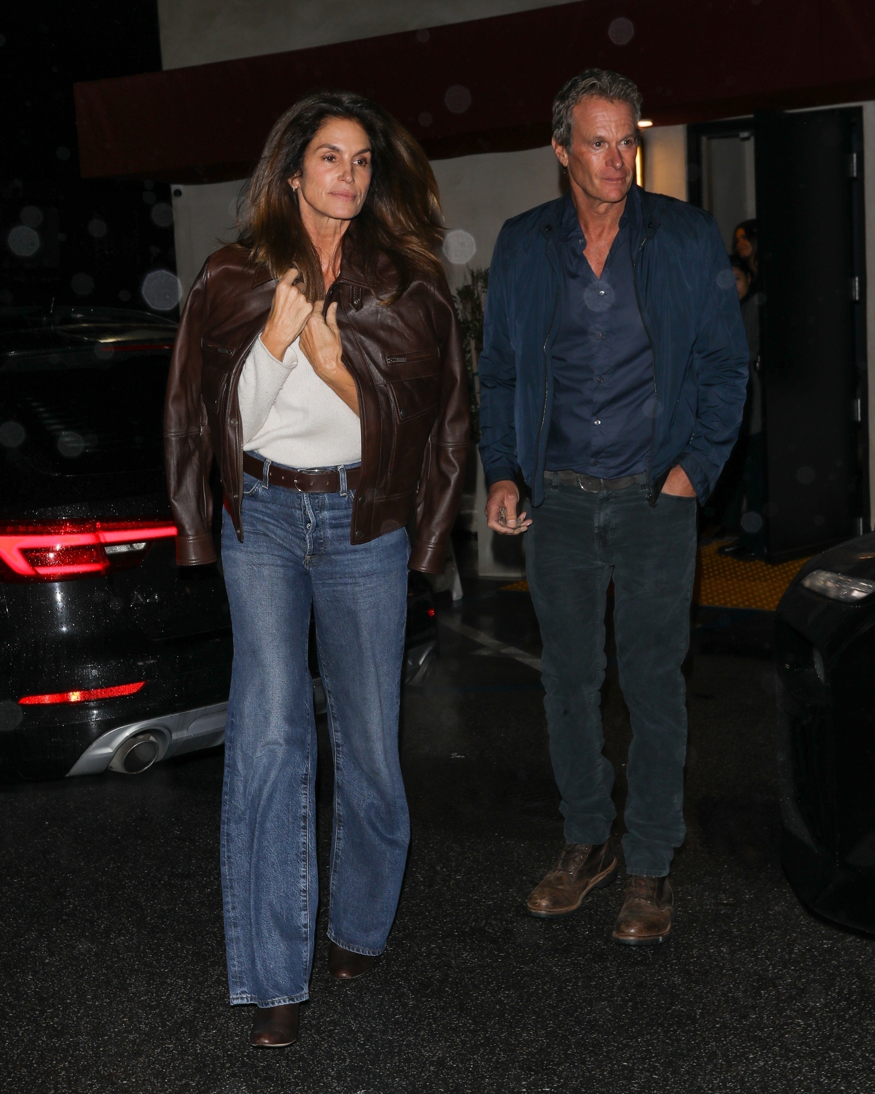 Cindy Crawford wearing a brown leather jacket, white top, and blue jeans